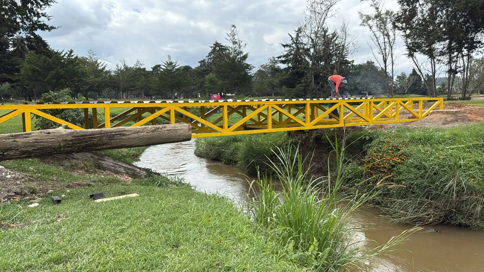 Puente peatonal metálico amarillo sobre una quebrada